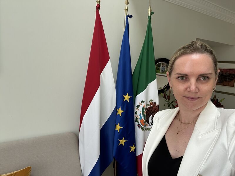 Julie Aubin à l’ambassade du Royaume des Pays-Bas au Mexique, devant les drapeaux néerlandais, européen et mexicain